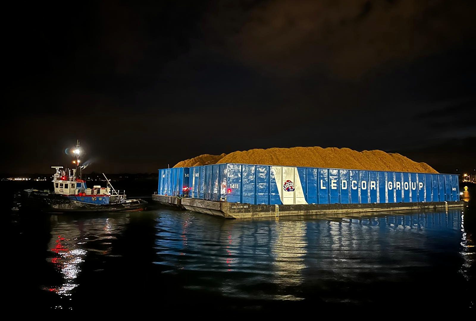 A tug pushing a loaded barge across the water at night