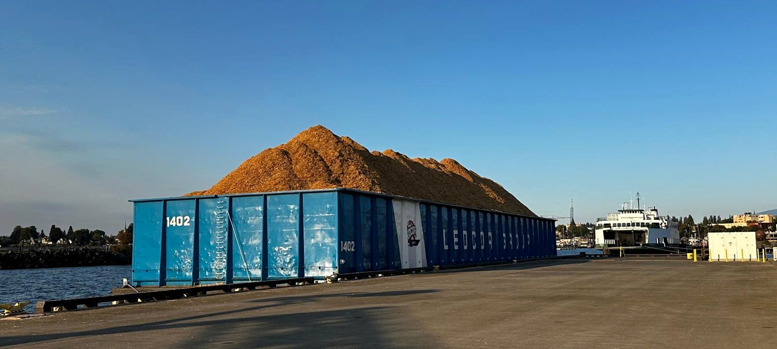 A loaded chip barge moored alongside a bulk terminal under a clear sky
